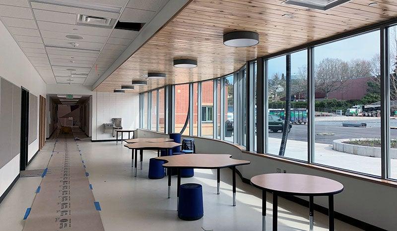 a hallway with tables in front of a curving wall of windows on the left